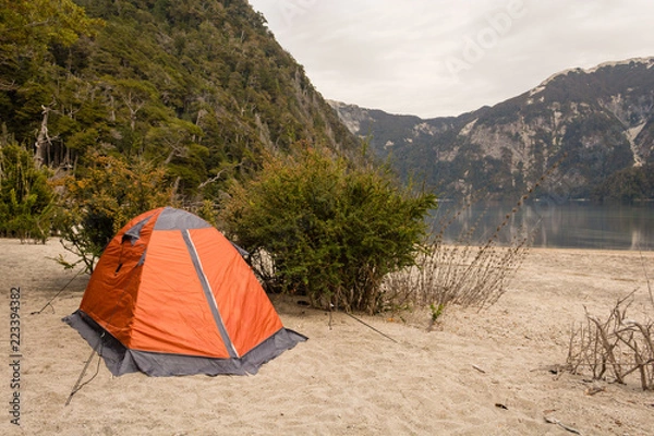 Fototapeta Camping orange tent in a campsite near a lagoon / Camping gear / Camping on the beach next to a lake with cloudy sky