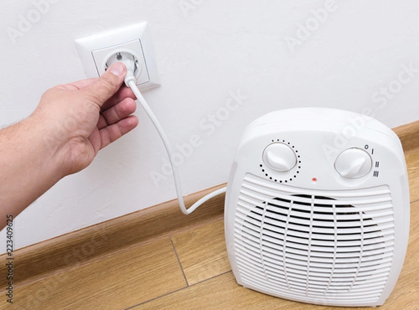 Obraz Person's hand plug in electric heater in the socket