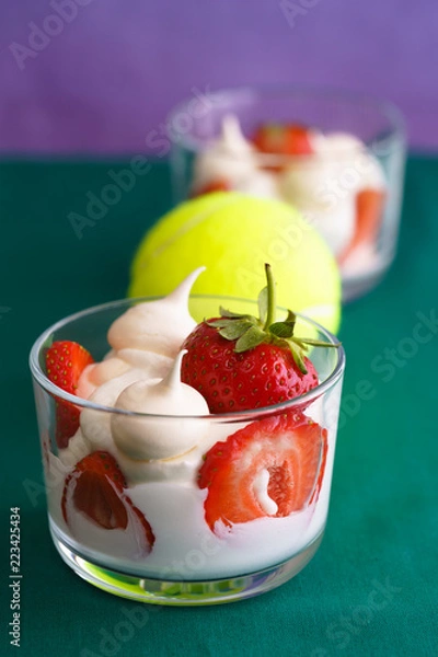 Fototapeta Wimbledon inspired whipped cream, meringues and fresh strawberries in a glass bowl on a green and violet background with a tennis ball