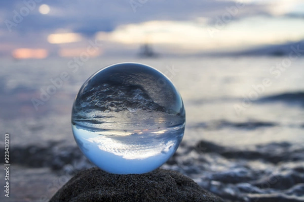 Fototapeta Fala na plaży i łodzie na horyzoncie o zachodzie słońca w szklanej kuli
