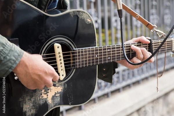 Fototapeta A side and close-up view in the afternoon of a mixed race man playing your guitar in the street. Music, culture, urban and people as a concept