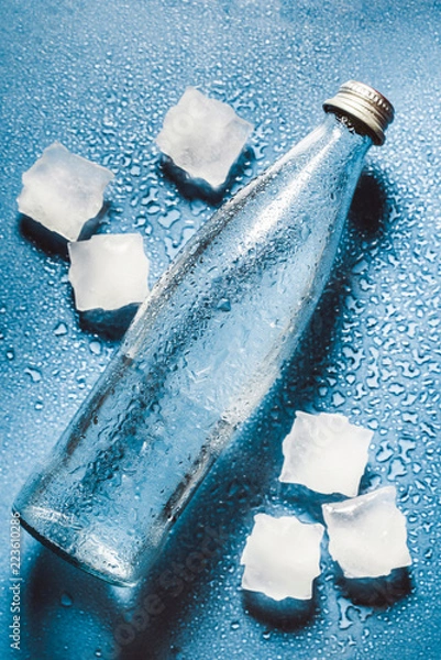 Obraz Glass water bottles on blue background splash water drops on top and cubes . Quench thirst. Background of water drops