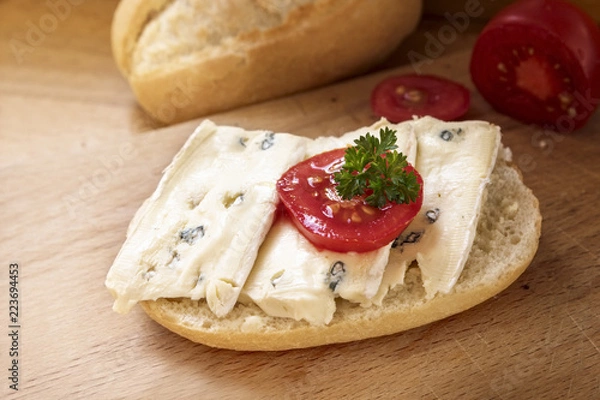 Fototapeta bread roll with mould cheese, tomato and parsley garnish on a wooden table