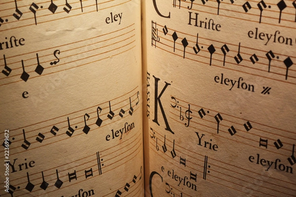 Fototapeta An old score written on a parchment, showing a few staves with notes and a miniature, for a song in Latin