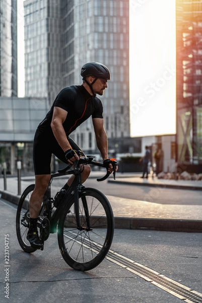 Obraz Cyclist riding professional bike next to modern buildings and skyscrapers.