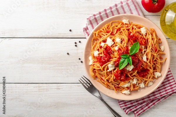 Fototapeta Spaghetti pasta with tomato sauce, mozzarella cheese and fresh basil in plate on white wooden background. Top view. Copy space.