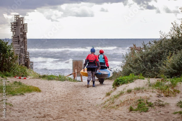 Fototapeta спортсмены несут лодку по песчаному пляжу к морю
