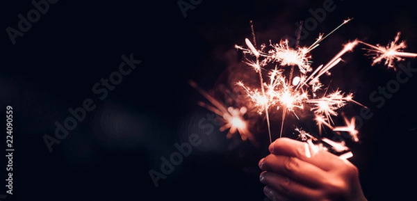 Obraz Ręka trzyma płonący wybuch brylant na czarnym tle bokeh w nocy, impreza uroczystości wakacje, ciemny ton vintage