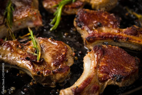 Obraz Closeup of Lamb chops frying in a rustic metal pan with rosemary and mixed pepper