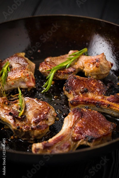 Obraz Lamb chops frying in a rustic metal pan with rosemary and mixed pepper