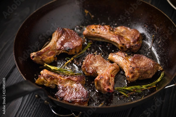 Obraz Lamb chops frying in a rustic metal pan with rosemary and mixed pepper