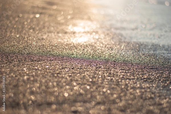 Fototapeta Sandy beach in the rays of sunset and surf, blurred background with the effect of dispersion from lenses