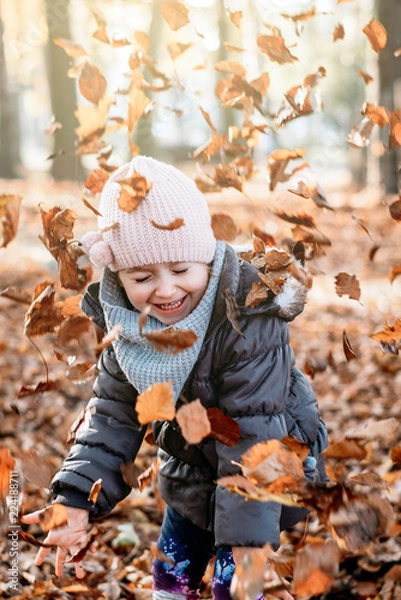 Fototapeta child is playing with leaves that have fallen from the tree