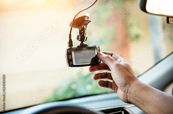 Fototapeta The human hand is touching the CCTV car camera,for check system before use,the technology for car user,for safe and secure driving,warm light tone,blurry light around