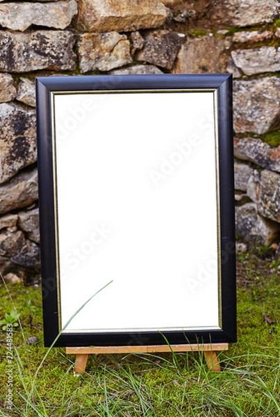 Fototapeta Easel staying om grass and moss near ancient stone walll with copy space