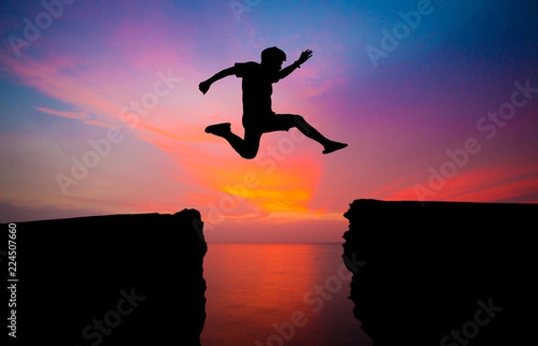 Fototapeta man jump over through on the gap of hill silhouette light, blue sky and sun on background.image for spirit and brave concept.spirit man is representative of success in the past and gold for the future