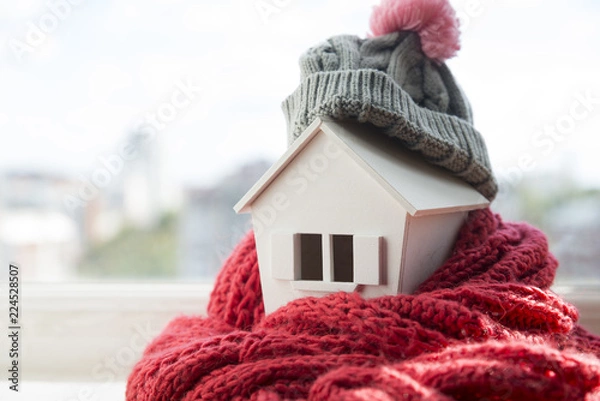 Fototapeta house in winter - heating system concept and cold snowy weather with model of a house wearing a knitted cap