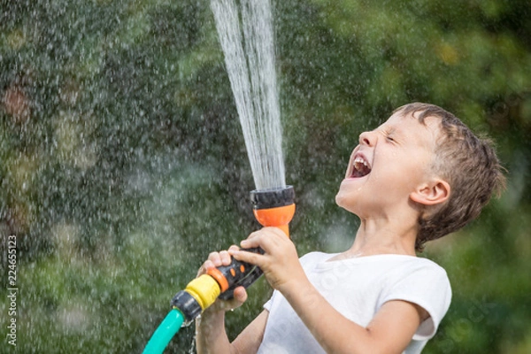 Fototapeta Happy little boy pouring water from a hose.