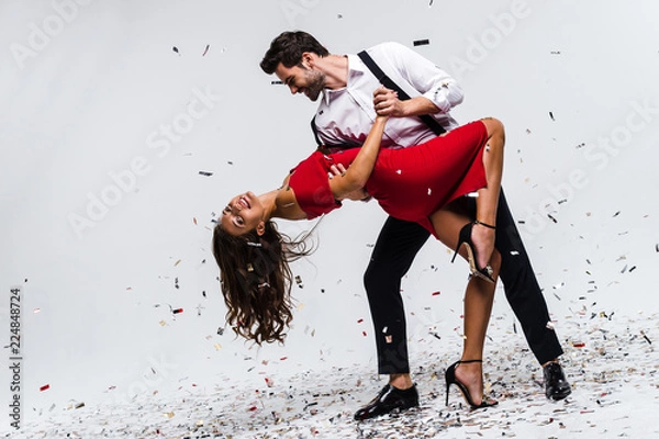 Fototapeta To jest gorąca salsa! Pełna długość młody piękny para taniec podczas gdy stojący przeciw białemu tłu z confetti