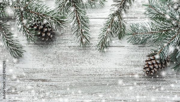 Fototapeta Christmas theme with fir branches, cones, globes, on white wooden background viewed from above, in snow, greeting card with space for text