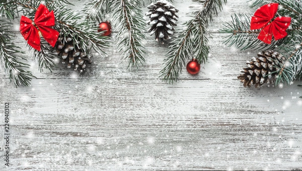 Fototapeta Christmas theme with fir branches, cones, globes, red bows on white wooden background viewed from above, in snow, greeting card with space for text