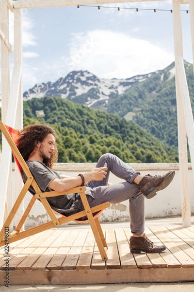 Fototapeta man sitting in chair using phone with mountains on background