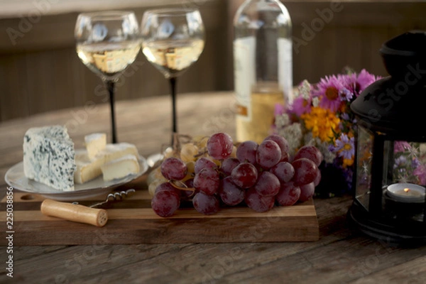 Fototapeta wine in a bottle,a glasses of white wine, grapes,various cheese and ,blue cheese,cheese Camembert, a bouquet and a lantern on the old table