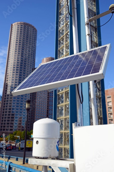 Fototapeta Solar panel in urban environment with buildings and skyscrapers in background with blue sky