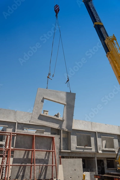Fototapeta Construction site crane is lifting a precast concrete wall panel.