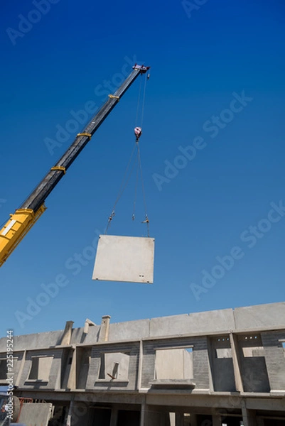 Fototapeta Construction site crane is lifting a precast concrete wall panel.