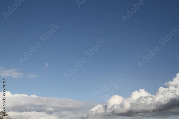Fototapeta A blue sky with the moon and various formations of cloud at the bottom.