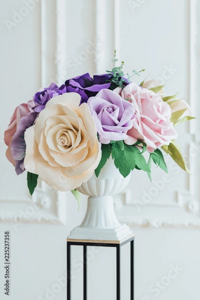 Fototapeta Beautiful decor for wedding. Composition of flowers and greenery in banquet hall, white tall vase, against white background. Luxury flower bouquet