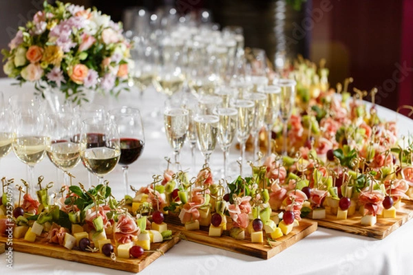 Fototapeta the buffet at the reception. Glasses of wine and champagne. Assortment of canapes on wooden board. Banquet service. catering food, snacks with cheese, jamon, prosciutto and fruit