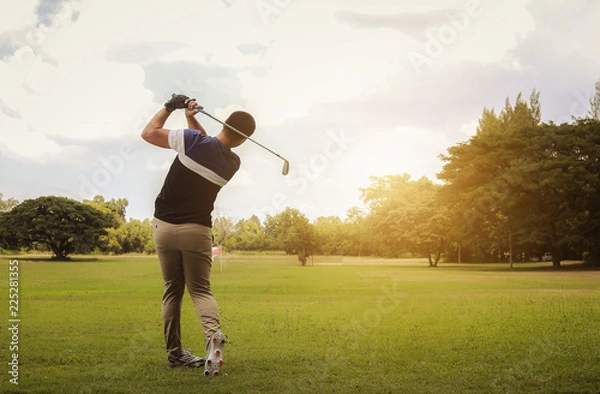 Fototapeta Golfer hitting golf shot with club on course at evening time.