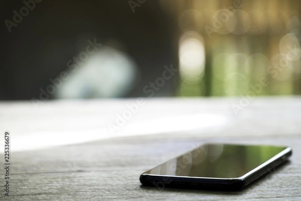 Obraz black charging mobile phone on the wooden table on blured nature background.