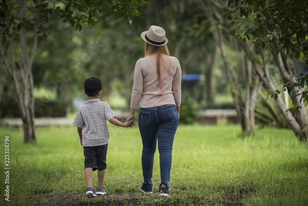 Fototapeta Rear view of mother and son walking together in home garden holding hand. Family concept.
