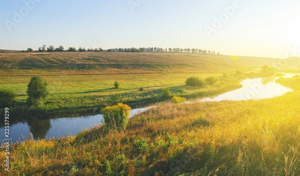 Fototapeta Sunny summer landscape with river flowing between the beautiful green hills,fields and meadows.