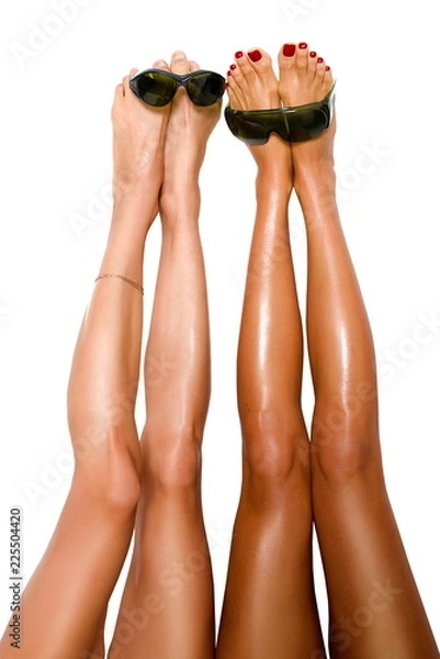 Obraz two beautiful pairs of smooth woman's legs after laser hair removal with protection glasses for laser removal on the white background