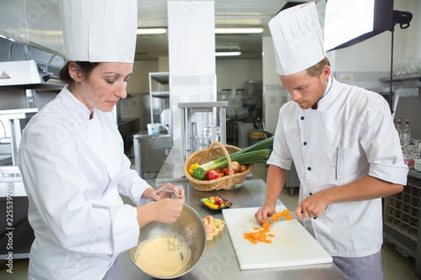 Obraz szczęśliwi szefowie kuchni i asystent w fartuchu pracujący w kuchni restauracji