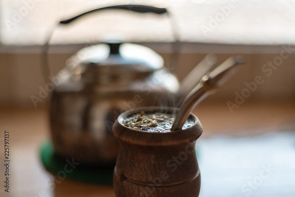 Fototapeta Filled smoking mate with a kettle on a watermelon trivet over a wooden counter and half window on the background