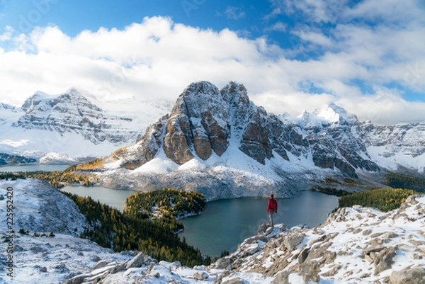 Fototapeta A lone man in a red jacket watches a cloud covered peak