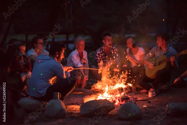 Fototapeta young friends relaxing around campfire