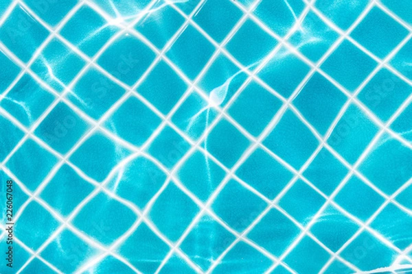 Fototapeta Blue tile on swimming pool bottom under clear water with sun light reflection. Travel, vacation concept. Text space.