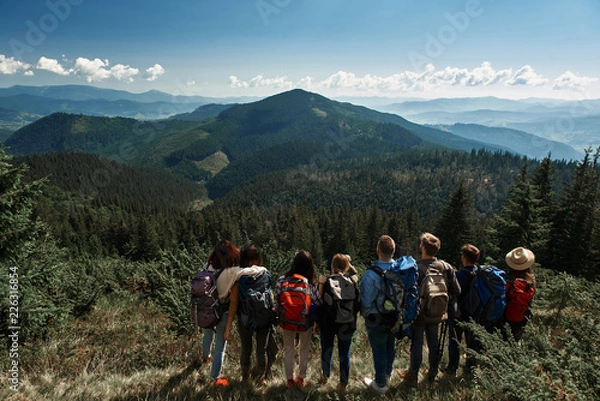 Fototapeta Panoramic view of the Carpathian mountains covered with deep forest with a group of tourists standing on the mountain hill