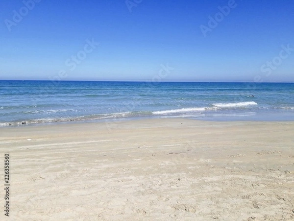 Obraz Empty sand beach with blue sea and blue sky background.