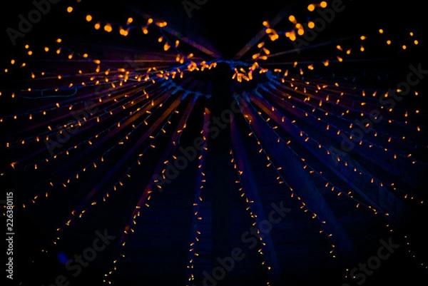 Fototapeta A collection of small little orange lights on the top of a purple ceiling of a tent at a wedding at night in the UK