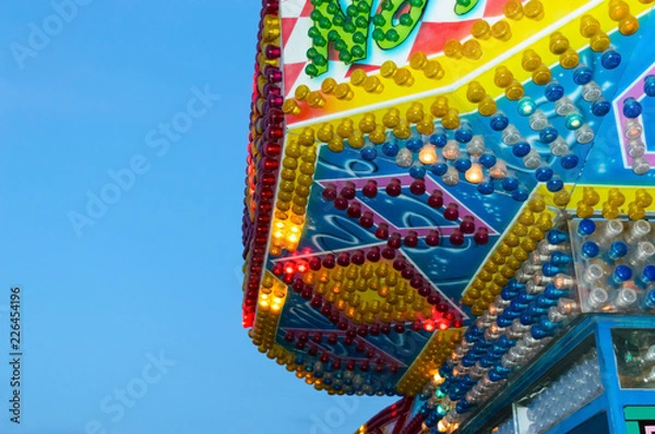 Fototapeta Amusement park. Beautiful bright building with burning lights close-up against the blue sky.