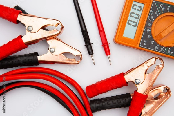 Fototapeta Jump start crocodile clip wire clamps for recharge battery car and Multimeter isolated on white desk