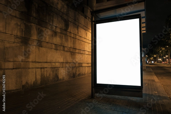 Fototapeta Light box with white blank space for ads at bus stop and wall in background. Night street marketing concept. Horizontal mock-up