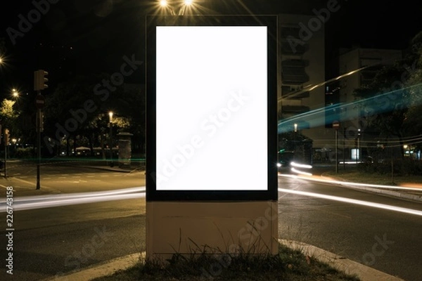 Fototapeta Light box with white blank space for advertisement at road intersection. Night street urban mockup concept with car light trails. 
